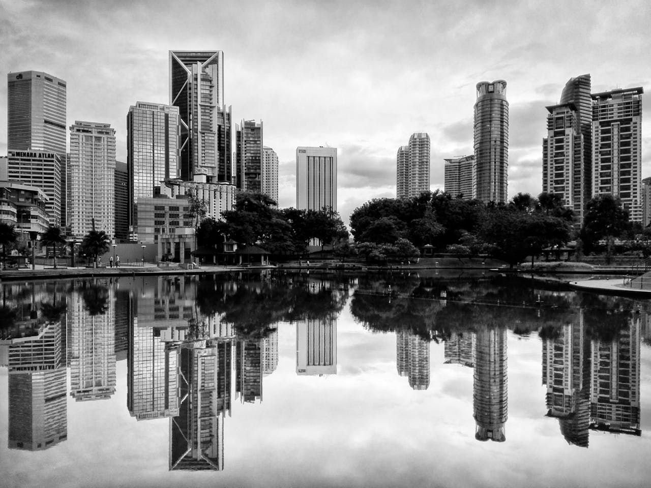 Monochrome view of Kuala Lumpur's modern skyline reflected in serene water.
